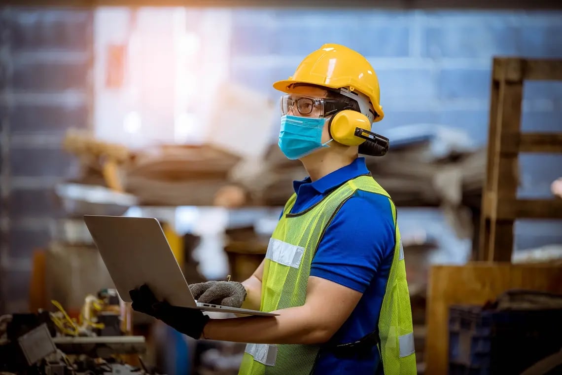 industrial-worker-full-ppe-laptop-warehouse